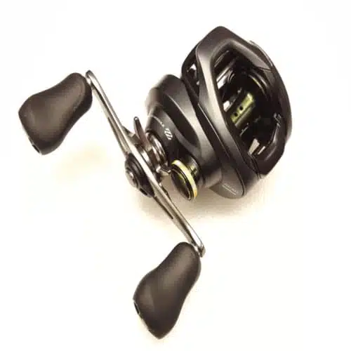 El Carrete Shimano Curado Cu201 Left Hand Cu201hgk, un carrete de pesca con baitcasting negro y plateado con dos manivelas, parece estar hecho de metal y cuenta con empuñaduras ergonómicas. Su diseño compacto y elegante sugiere que es adecuado para la pesca de precisión, específicamente para uso con la mano izquierda. El carrete está fotografiado sobre un fondo blanco.