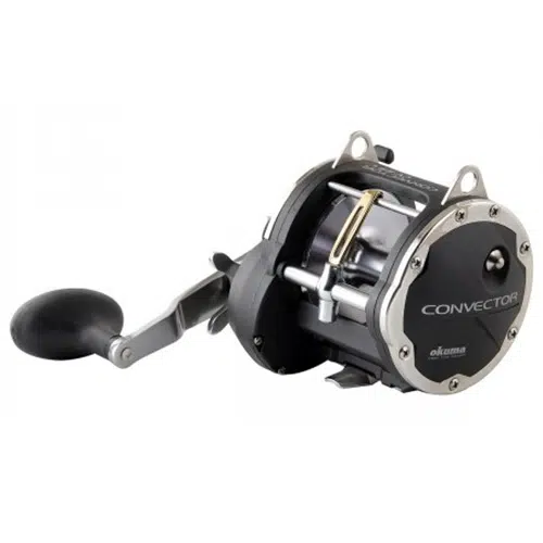 Se muestra un carrete de pesca Carrete Okuma Convector CV-55L de 560 m/0,50 mm, con un elegante diseño en plata y negro, sobre un fondo blanco. El carrete está equipado con un mango grande y una empuñadura redondeada, con el nombre de la marca "Okuma" y "Convector" claramente visible en el lateral.