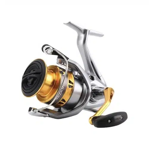 La imagen muestra un carrete de pesca elegante y moderno, el Carrete New Sedona 2500xg 160m/0,25mm Front Shimano, con un acabado plateado y dorado. El carrete cuenta con un mango negro y detalles intrincados, diseñado para la pesca de precisión. El cuerpo compacto sugiere que es liviano y fácil de usar.