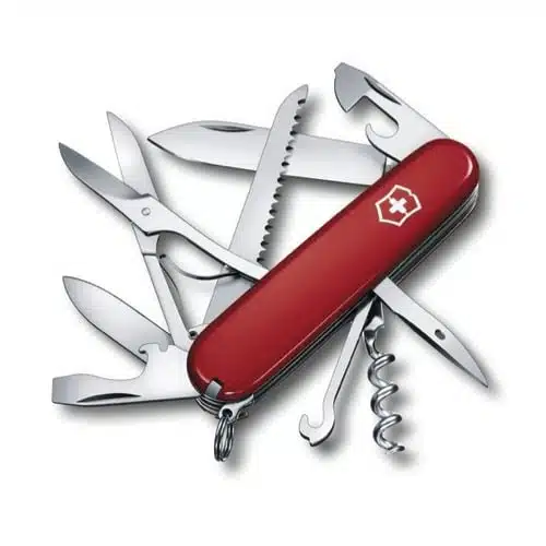 La navaja suiza roja Cortapluma Huntsman Victorinox 1.3713 presenta varias herramientas extendidas, entre ellas una hoja de cuchillo, tijeras, una sierra, un abrelatas, un sacacorchos y un abridor de botellas. El mango de la navaja presenta un emblema de cruz blanca.