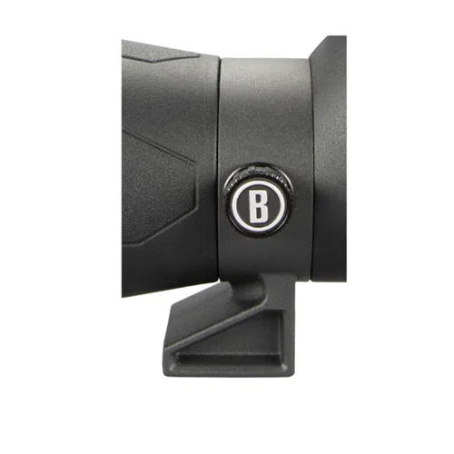 Primer plano de una sección del telescopio Spotter Bushnell Engage 20-60x80mm, que presenta un pequeño emblema circular con la letra "B" en el centro. El dispositivo tiene un diseño texturizado y un soporte de montaje debajo del emblema. El fondo es blanco.