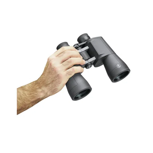 La mano izquierda de una persona sostiene un par de binoculares Binocular Powerview2 20x50mm de Bushnell. Los binoculares negros tienen empuñaduras texturizadas y perillas de enfoque ajustables, con las lentes orientadas hacia abajo. El fondo blanco ofrece un claro contraste entre los binoculares y la mano.