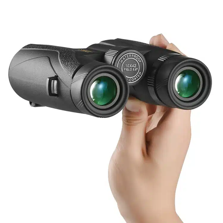 Una persona sostiene un par de binoculares Comet 10x42 W04-1042, destacando su exterior negro y su cómodo agarre. Las lentes de color verde, marcadas con sus especificaciones de resistencia al agua, lo hacen ideal para los exploradores ávidos.