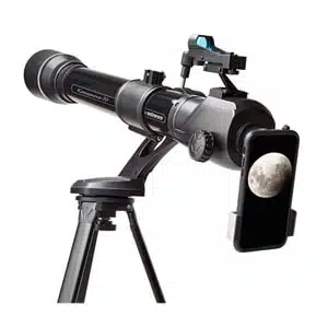 Un telescopio refractor Konus Konusnova 70 70x80mm #1755 está montado en un trípode con un teléfono inteligente conectado, mostrando una imagen clara de la luna. El telescopio incluye varios controles y un dispositivo de observación en la parte superior, colocado sobre un fondo blanco liso.