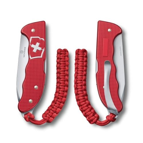 La Cortapluma Hunter Pro Alox Rojo Victorinox 0.9415.20 presenta una hoja plegable y un mango de paracord en un rojo vibrante, que se muestra desde dos ángulos: cerrado y abierto. Este modelo presenta de manera prominente un emblema de cruz blanca en el mango texturizado.