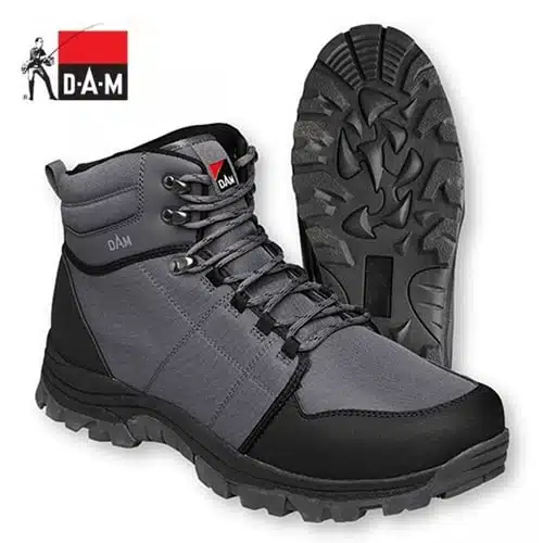 Un par de botas de senderismo Zapato Vadeo Dam Iconiq Cleated Gris con diseño en gris y negro y suelas gruesas y resistentes con tacos, diseñadas específicamente para uso en exteriores. La marca "DAM" se muestra de forma destacada en la lengüeta y el talón. Una bota está en posición vertical, mientras que la otra muestra el dibujo de la banda de rodadura. Además, se puede ver un pequeño logotipo de D.A.M. en la esquina superior izquierda.