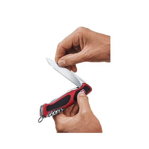 Se muestran dos manos, una de ellas sostiene un Cortapluma Victorinox Ranger Grip 55 #0.9563.C en rojo y negro, mientras que la otra abre con cuidado la hoja principal. El cuchillo tiene una hoja brillante y afilada e incluye un llavero en un extremo.