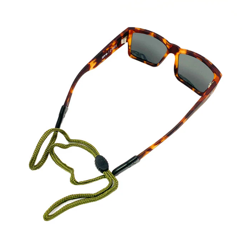Las gafas de sol Strap Lentes Cordón Uki Verde son de carey con lentes orientadas hacia adelante, equipadas con lentes Uki Verde y un cordón verde unido a las patillas. El cierre negro ajustable asegura las gafas de sol alrededor del cuello.