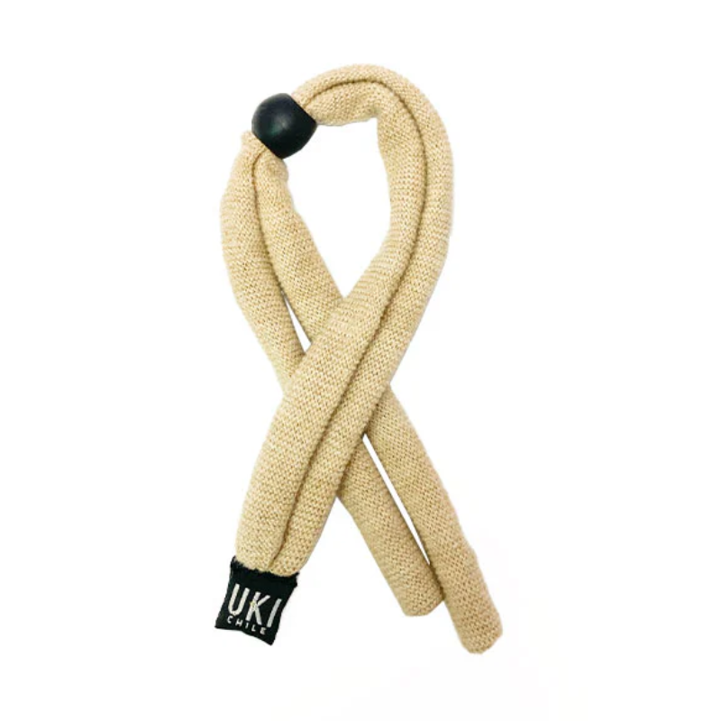 La Correa Lentes Género Uki Beige es un accesorio para el cabello texturizado de color beige que se cierra con un elegante lazo con una cuenta negra en la parte superior. Tiene una etiqueta negra que dice "Género UKI" en la parte inferior, lo que le da un toque de estilo único.