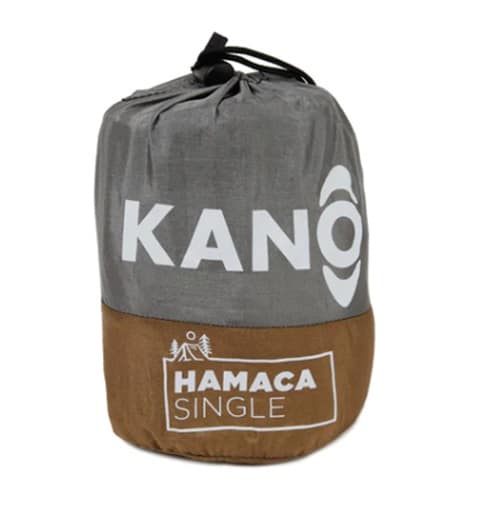 Una bolsa con cordón gris y marrón muestra la marca "Hamaca Single Kaki Kano", con "KANO" impreso en blanco en la sección superior. Debajo, las palabras "HAMACA SINGLE" se presentan elegantemente junto a un gráfico de un árbol, lo que representa la filosofía de diseño de Kaki Kano.