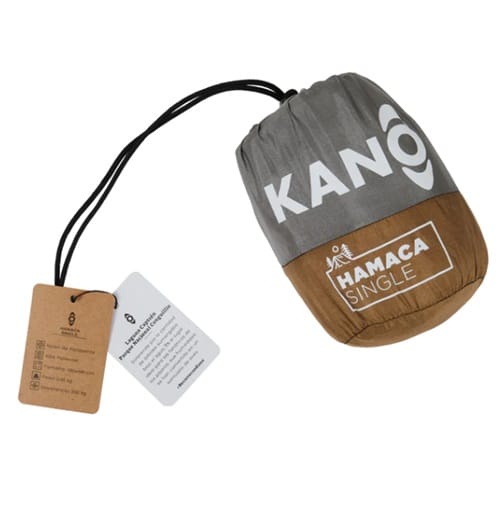 La "Hamaca Single Kaki Kano" es una hamaca compacta de color marrón y gris diseñada por expertos de Kaki Kano, que se guarda cuidadosamente en una bolsa con cordón. Incluye dos etiquetas con información del producto, lo que lo prepara perfectamente para su próxima aventura de relajación.