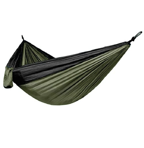 La hamaca Single Verde Camo Kano, que presenta una tela de nailon verde oliva y negra con un patrón de camuflaje, se cuelga y se exhibe sobre un fondo blanco. El material de dos tonos de la hamaca se frunce en los extremos, formando un amplio cabestrillo para descansar.