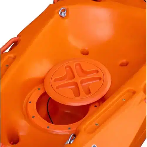 Primer plano de un kayak Marimba Vagabond en color naranja, que muestra una tapa de escotilla circular con un diseño en forma de cruz. La superficie del kayak es lisa, presenta fijaciones de pernos visibles y una escotilla parcialmente abierta.