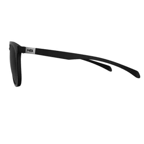 Un par de lentes de sol Burnie Hot Buttered en color negro, con marcos rectangulares y patillas delgadas y rectas. La patilla izquierda está decorada con un pequeño emblema plateado cerca de la bisagra. Estas gafas de sol ofrecen lentes oscuras y cuentan con un diseño elegante y moderno, ideal para lograr un look elegante bajo el sol.