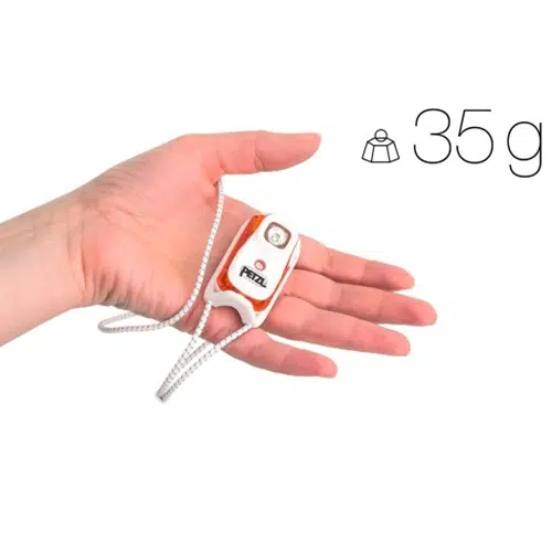 Una mano que sostiene una linterna frontal Petzl Bindi 200lm compacta y ligera con correa, que pesa solo 35 gramos. La pequeña linterna cabe cómodamente en la palma de la mano.