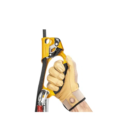 Una persona con guantes color canela sujeta un bloqueador Petzl Ascension Izquierdo de color amarillo, que está unido a una cuerda negra. El equipo incluye un mosquetón conectado al bloqueador para garantizar la seguridad durante la escalada, lo que garantiza un soporte fiable y seguro durante el ascenso.