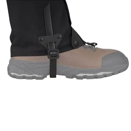 Primer plano de una persona que lleva una bota beige y gris, combinada con las polainas Polainas Sea To Summit Quagmire Canvas (SIN PFC) M en color negro. La bota duradera cuenta con una suela gruesa, mientras que la polaina de lona sin PFC se ajusta de forma segura alrededor del tobillo con una correa y una hebilla.