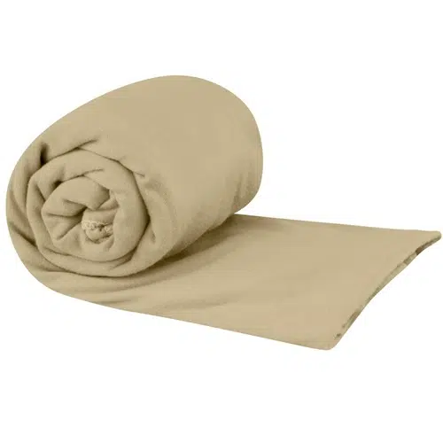 Una manta de vellón marrón claro enrollada está parcialmente desenrollada, revelando su textura suave y lisa. La manta, al igual que la Toalla Microfibra Sea To Summit Pocket Towel Medium, parece acogedora y adecuada para brindar calidez.