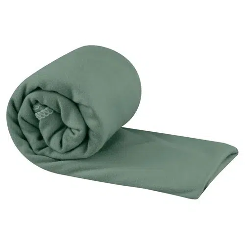 Una manta de polar verde cuidadosamente enrollada, con un extremo ligeramente desenrollado y que se extiende hacia afuera, se encuentra junto a una Toalla Microfibra Sea To Summit Pocket Towel Small. La manta tiene una textura suave y se ve acogedora y cómoda.