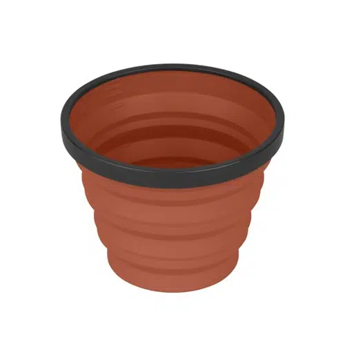 Ilustración de un recipiente de silicona plegable, redondo y de color terracota con borde negro. El recipiente parece tener una textura estriada que permite plegarlo para guardarlo de forma compacta.