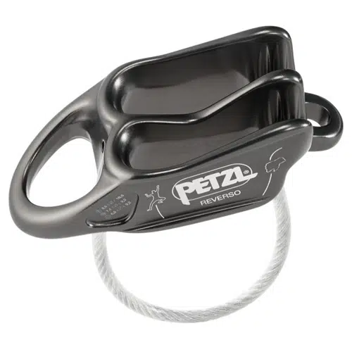 Dispositivo de aseguramiento Petzl Reverso Gris de color gris oscuro, con dos ranuras para cuerdas de aseguramiento y un orificio de fijación. El dispositivo se muestra con un alambre metálico enrollado. El logotipo de Petzl y una pequeña ilustración son visibles en el lateral.