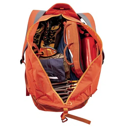 Una mochila naranja abierta revela un contenido organizado: una botella de agua roja, ropa doblada, un par de bastones de senderismo, un estuche naranja para el Bolso para Cuerda Petzl Kliff y otros equipos perfectamente embalados y adecuados para actividades al aire libre.
