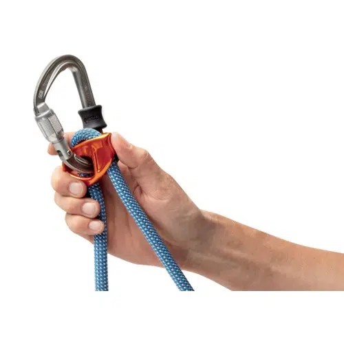 Una mano sostiene una cuerda azul que pasa por un dispositivo de seguridad de escalada naranja, conectado a un mosquetón plateado. El equipo incluye el versátil Cabo de Anclaje Regulable Petzl Connect Adjust. Sobre un fondo blanco liso, el diseño elegante del equipo se destaca.