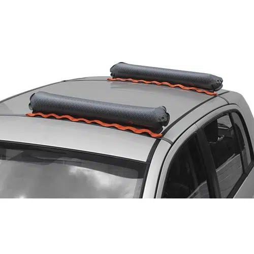 Primer plano del techo de un automóvil gris equipado con dos almohadillas cilíndricas, anaranjadas y negras, suaves para portaequipajes inflable Sea To Summit Pack Rack, colocadas en la parte superior. Las almohadillas para portaequipajes parecen estar diseñadas para transportar elementos como tablas de surf o kayaks mientras protegen el techo del automóvil.