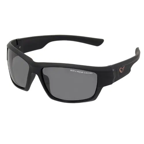 Un par de elegantes gafas de sol deportivas envolventes de color gris oscuro con lentes tintadas oscuras. La patilla izquierda tiene el logotipo "Savage Gear", mientras que la patilla derecha presenta el emblema estilizado de la marca. Estas Lentes de Sol Polarizados Savage Dark Grey tienen un diseño moderno y resistente, perfecto para cualquier actividad al aire libre.