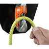 Una mano pasa con destreza una cuerda de escalada de color verde amarillento por un dispositivo de seguridad naranja y plateado con la inscripción "PETZL", que muestra el Mosquetón Petzl con Base Easytop Wall sobre un fondo oscuro. Esta disposición resalta la importancia de contar con un equipo de seguridad de alta calidad para la escalada.