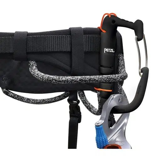 Primer plano de un arnés Arnés Petzl Aquila negro con bloqueador y mosquetón de marca Petzl acoplados. Una cuerda texturizada en blanco y negro pasa por el arnés, lo que proporciona sujeción y seguridad para las actividades de escalada.