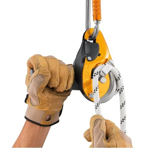 Una persona con guantes color canela opera un Descensor Industrial Petzl Autofrenante ID Evac con una cuerda conectada. El dispositivo es amarillo y negro, mientras que la cuerda es blanca con marcas negras, lo que indica su uso para escalar o levantar objetos.
