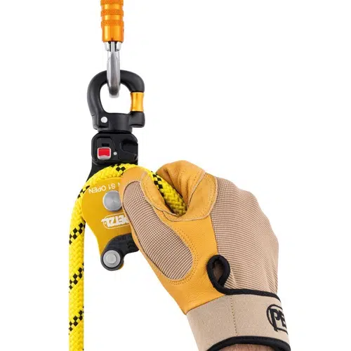 Una mano enguantada sujeta una cuerda de escalada amarilla y negra conectada a un dispositivo Polea Industrial Simple Petzl Spin S1 Open con un mosquetón. El dispositivo naranja y negro lleva la marca "Petzl". El guante marrón y tostado también lleva el logotipo "Petzl" en la muñeca, lo que garantiza la seguridad en cada aventura de escalada.