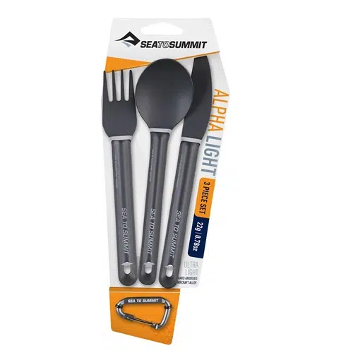 El Set de Cocina Sea To Summit Alpha Light 3pc es un conjunto de utensilios de camping negros de la marca Sea to Summit. Incluye un tenedor, una cuchara y un cuchillo con las etiquetas "Alpha Light 3-Piece Set" y "Ultra Light". También se incluye un mosquetón plateado en el paquete.