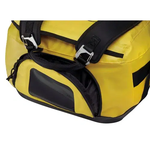 Primer plano de una bolsa Petzl Duffle 85 amarilla y negra con una ventana de identificación transparente y asas negras resistentes. La bolsa tiene cierres de metal y detalles de cremallera. El material parece duradero e impermeable, ideal para uso al aire libre o de viaje.
