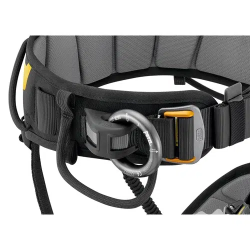 Primer plano de un arnés de escalada negro y gris con hebillas y presillas de metal. Cuenta con correas ajustables y un mosquetón conectado al portamaterial Punto de Enganche Petzl Ring2Side. El arnés, ideal para actividades en ángulos altos, incorpora la tecnología Ring2Side de Petzl para una mayor seguridad y versatilidad.