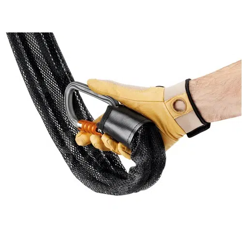 Una mano que lleva un guante de color canela sujeta una cadena negra resistente, similar al duradero sistema Jag de Polipasto Petzl. Está revestida con una cubierta de malla y asegurada con un mecanismo de bloqueo metálico que incluye un componente naranja, que indica una mayor seguridad o cierre.