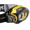 Un primer plano de la Linterna Frontal Petzl Pixa Z1 resalta su llamativo diseño en amarillo y negro, con dos lentes prominentes. La correa ajustable presenta de forma destacada el logotipo "Petzl". Esta linterna frontal está equipada con un dial etiquetado como "Off", lo que muestra un diseño robusto y compacto ideal para iluminación con manos libres.