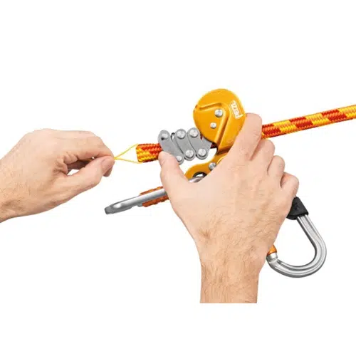 Manos que utilizan un dispositivo mecánico de agarre de cuerda amarillo-naranja para ajustar una cuerda de escalada Cuerda Semiestática roja y amarilla de 12,5 mm de grosor. Un mosquetón está conectado al dispositivo Petzl Control, diseñado para escalada o seguridad.