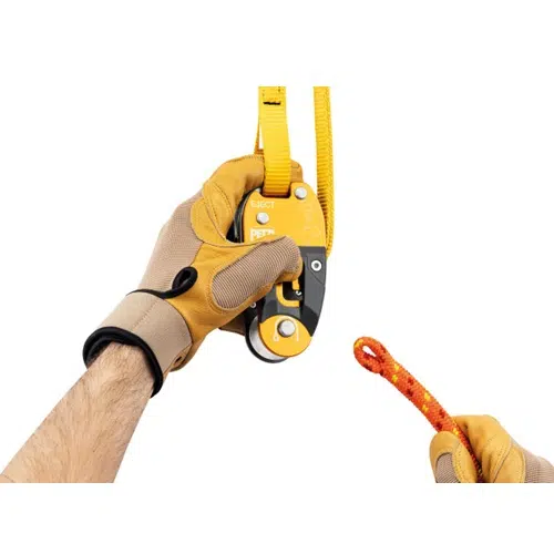 Una persona con guantes marrones maneja un dispositivo de aseguramiento Petzl GRIGRI amarillo y negro, con una correa amarilla. Agarra una cuerda naranja enrollada en un extremo, mostrando una configuración de escalada similar a la que se utiliza con el Salvarramas para Poda Petzl Eject en tareas de arboricultura.