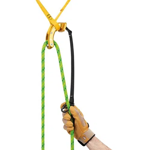 Una mano enguantada sostiene un dispositivo ascendedor sujeto a una cuerda de escalada amarilla. El dispositivo negro, con su distintiva empuñadura amarilla, armoniza a la perfección con la cuerda estampada en verde y amarillo, lo que lo convierte en una excelente opción para trabajos de escalada o arboricultura. Es especialmente eficaz cuando se utiliza con herramientas como el Salvarramas para Poda Naja de Petzl.