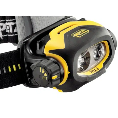 Primer plano de la linterna frontal Petzl Pixa 3 de 100 lúmenes que muestra su diseño en negro y amarillo con correas ajustables. Incluye luces LED duales que ofrecen 100 lúmenes de brillo y un dial lateral marcado como "Off" para un fácil control. El logotipo de Petzl se destaca de manera prominente en la parte superior.