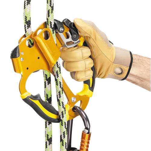 Una mano que lleva un guante de color canela sujeta el elegante Bloqueador Petzl Doble Ascentree, que está conectado a una cuerda de escalada negra, blanca y verde. El dispositivo está conectado de forma segura con un mosquetón para mayor seguridad durante la escalada.