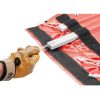 Una persona con un guante de cuero marrón tira de una cuerda atada a la Camilla para Rescates Petzl Nest. La tela roja y negra presenta ojales metálicos y cordones blancos, con una pieza metálica rectangular asegurada en ella, lo que la hace ideal para situaciones de emergencia.