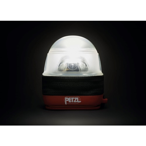 La linterna Petzl, con una base cilíndrica roja y negra, emite una luz blanca brillante desde su parte superior en forma de cúpula contra un fondo oscuro. La base tiene la etiqueta "Petzl" y está reforzada por el Estuche Difusor para Linterna Frontal Petzl Noctilight para una iluminación enfocada.