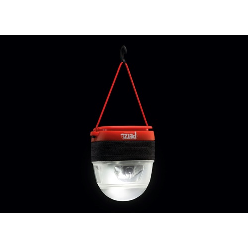 Un producto similar al Estuche Difusor para Linterna Frontal Petzl Noctilight presenta una linterna de camping portátil roja y negra con una mitad inferior transparente que revela una bombilla en su interior. Cuelga elegantemente de un cordón rojo con un gancho sobre un fondo negro.