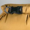 Primer plano de una bolsa impermeable Big River de color marrón amarillento de Bolsa Sea To Summit con una hebilla y correa de plástico negras. La hebilla con acabado mate tiene un texto grabado parcialmente visible, mientras que la tela presenta un patrón de cuadrícula sutil.