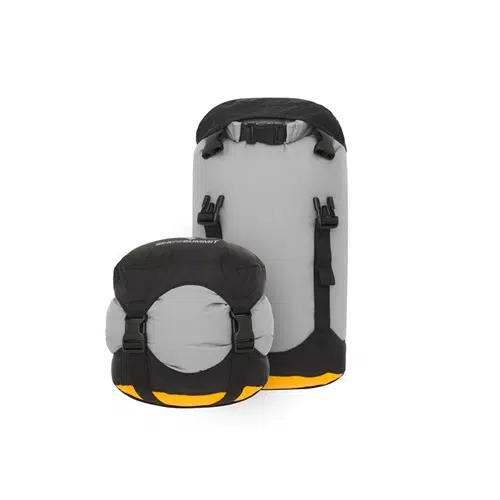 Se muestran dos bolsas de compresión secas Sea To Summit Evac Compression Dry Bags en gris y negro con detalles en naranja. Una bolsa está completamente extendida y la otra está compactada. Ambas bolsas cuentan con correas y hebillas ajustables para un cierre y compresión seguros, lo que las hace perfectas para sus necesidades de equipo.