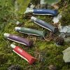 Cinco navajas de bolsillo de color vibrante Cuchillo Opinel N°8 Trekking con mangos de madera se exhiben sobre una roca cubierta de musgo en un entorno al aire libre. Las navajas, disponibles en tonos azul, verde, violeta, rojo y marrón, incluyen una correa de cuero. A su alrededor hay piñas y hojas pequeñas esparcidas.