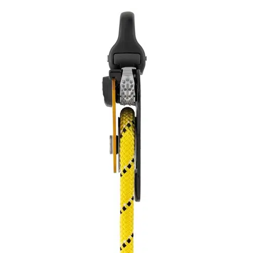 Primer plano de un Polea Industrial Petzl Pro Traxion sujetando una cuerda amarilla con rayas negras. Este dispositivo se asemeja a un bloqueador mecánico, diseñado para trabajos verticales con cuerda o asistencia en escalada, y garantiza un rendimiento eficiente y seguro en entornos difíciles.